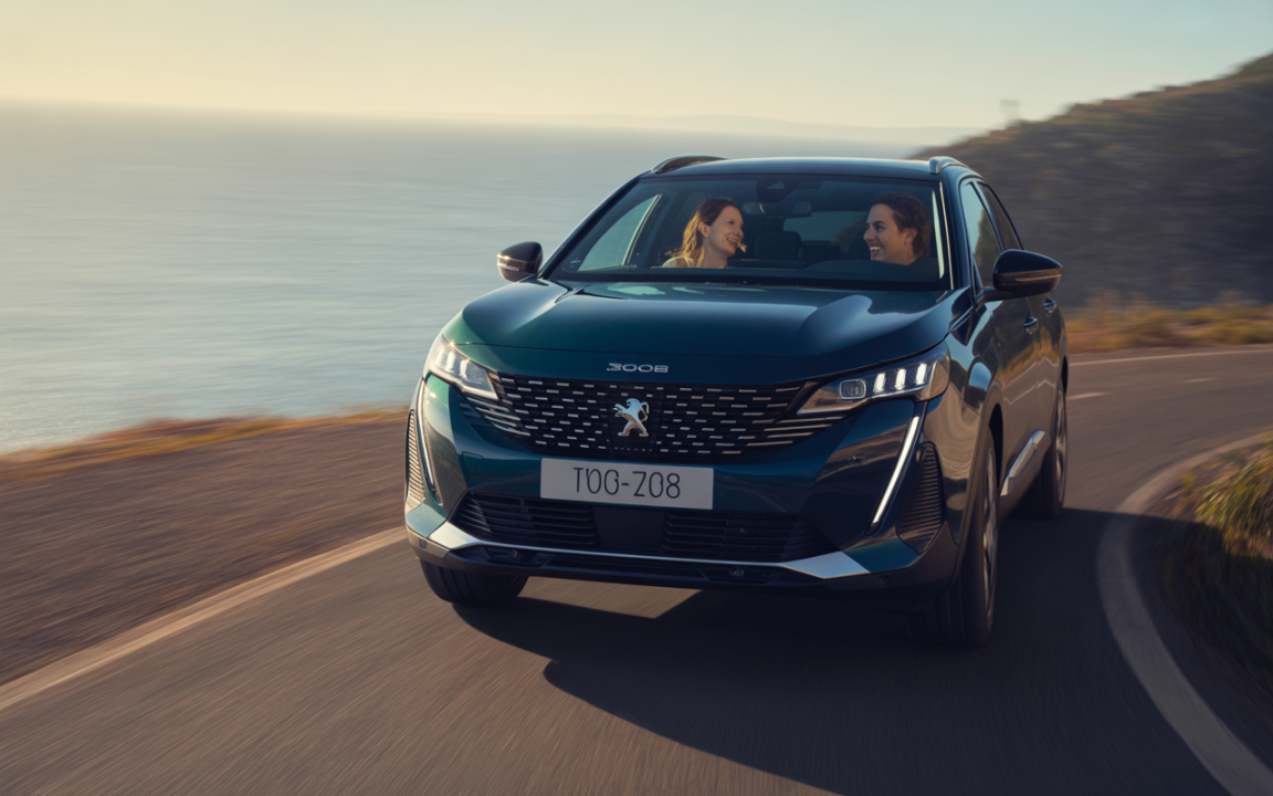 Une Peugeot 3008 roule le long d'une route côtière, avec deux passagers souriants à l'intérieur, sur fond de mer.