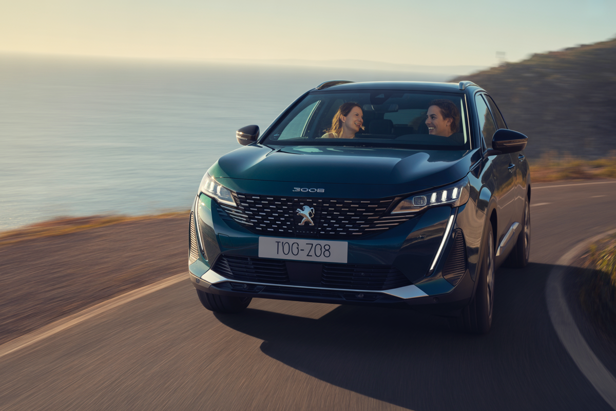 Une Peugeot 3008 roule le long d'une route côtière, avec deux passagers souriants à l'intérieur, sur fond de mer.