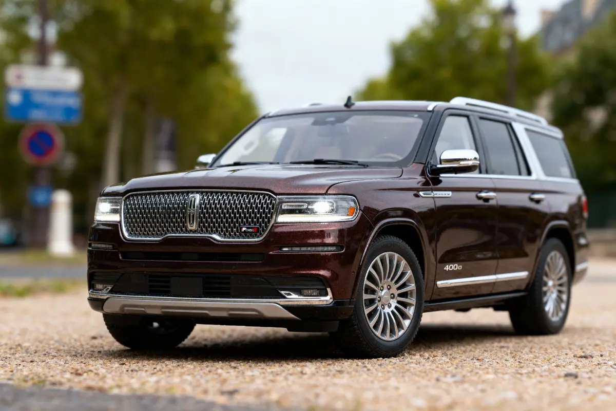 SUV marron stationné sur route en gravier, entouré d'arbres flous et panneaux en arrière-plan.