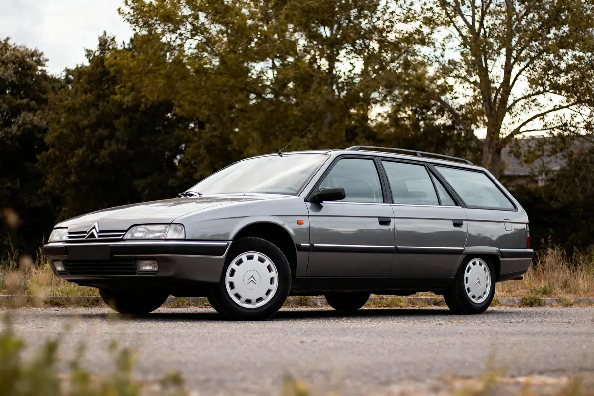 Voiture break grise Citroën stationnée sur la route, arbres en arrière-plan. Modèle vintage classique.