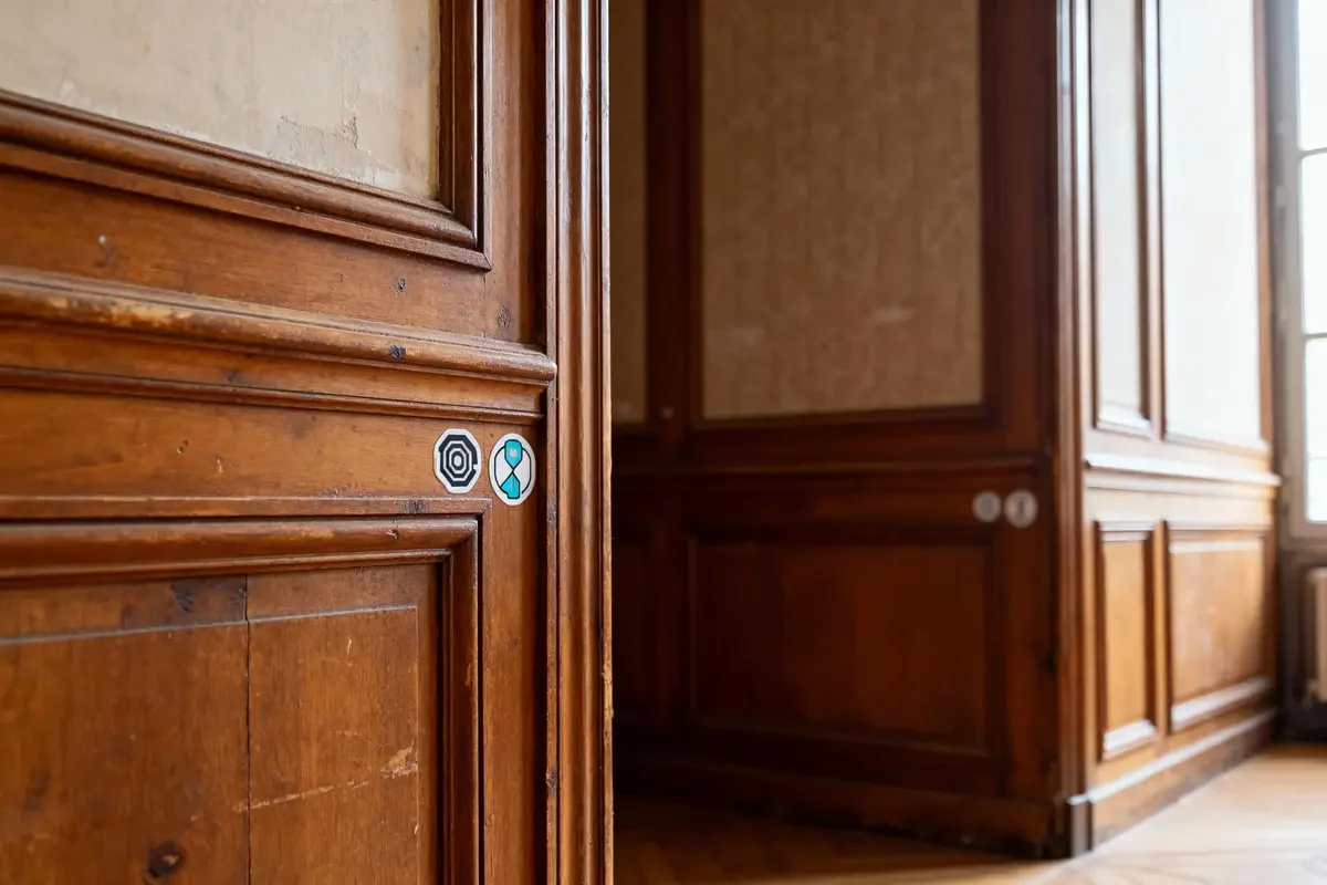 Porte en bois avec deux autocollants géométriques, intérieur d'une pièce lumineuse aux murs en boiseries.