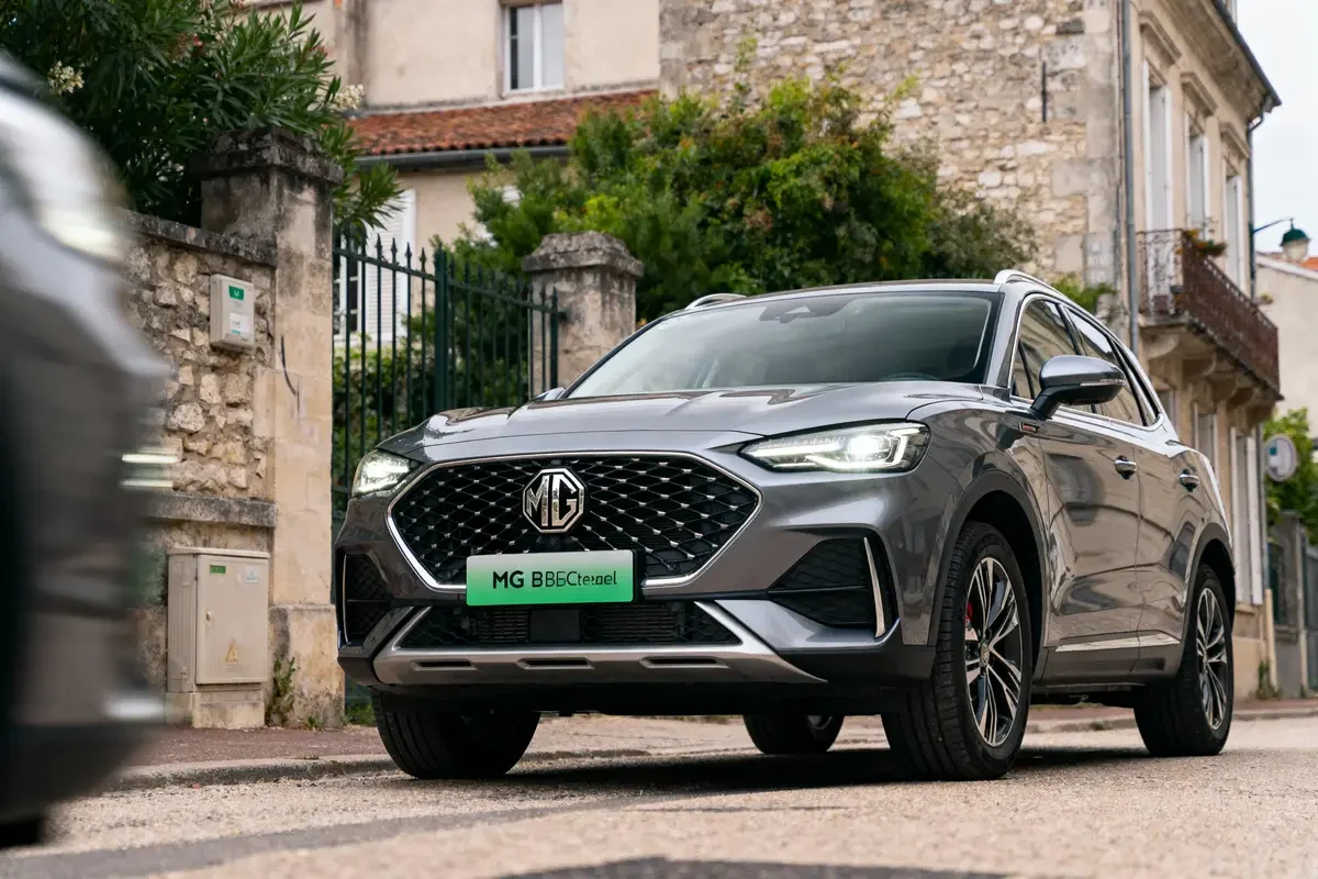 SUV gris MG garé devant une maison en pierre, rue pavée, environnement résidentiel.
