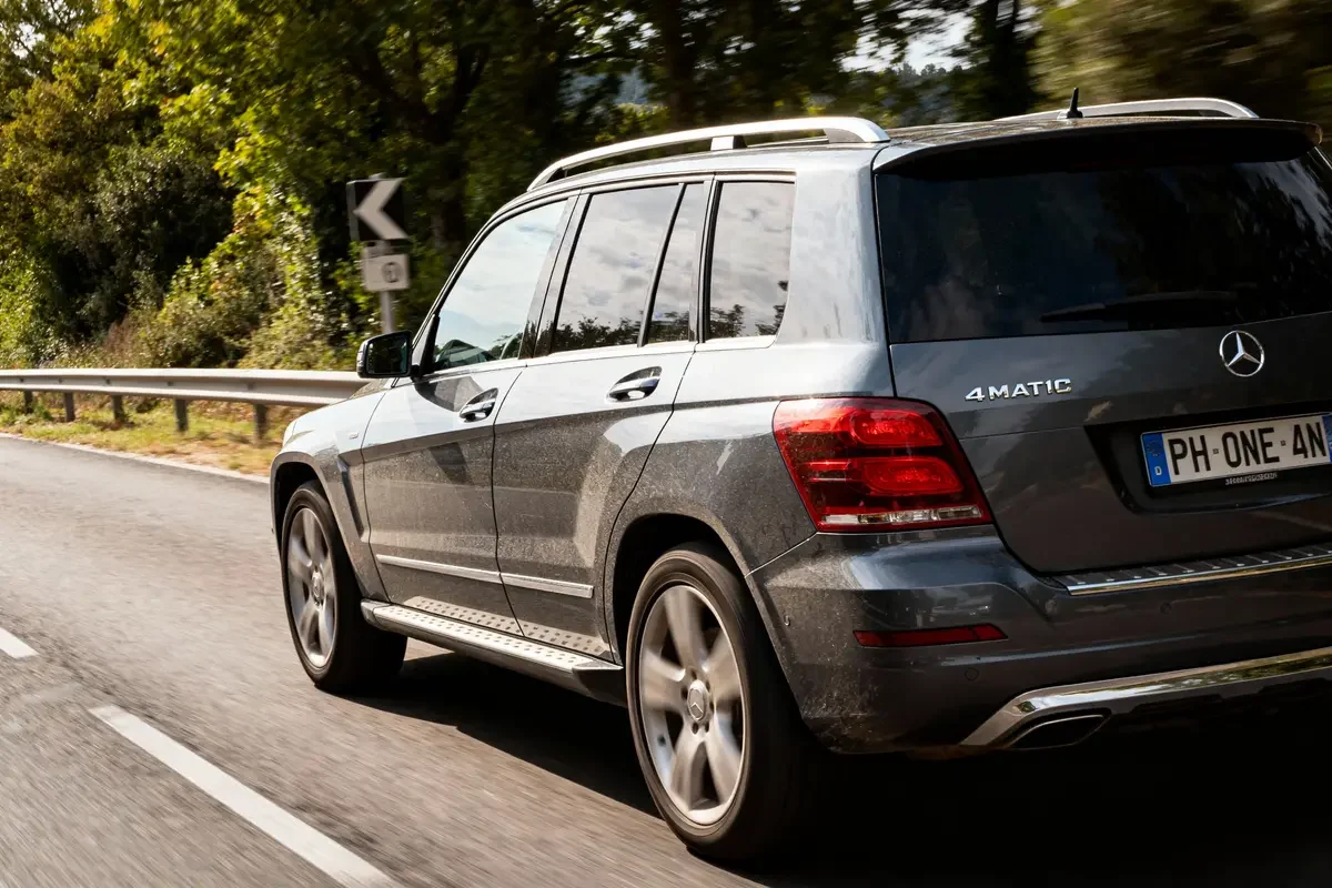 SUV gris Mercedes-Benz roulant sur route bordée d'arbres, immatriculation visible, par une journée ensoleillée.