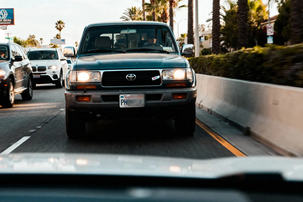 Voiture Toyota noire roulant sur une route urbaine bordée de palmiers et autres véhicules.