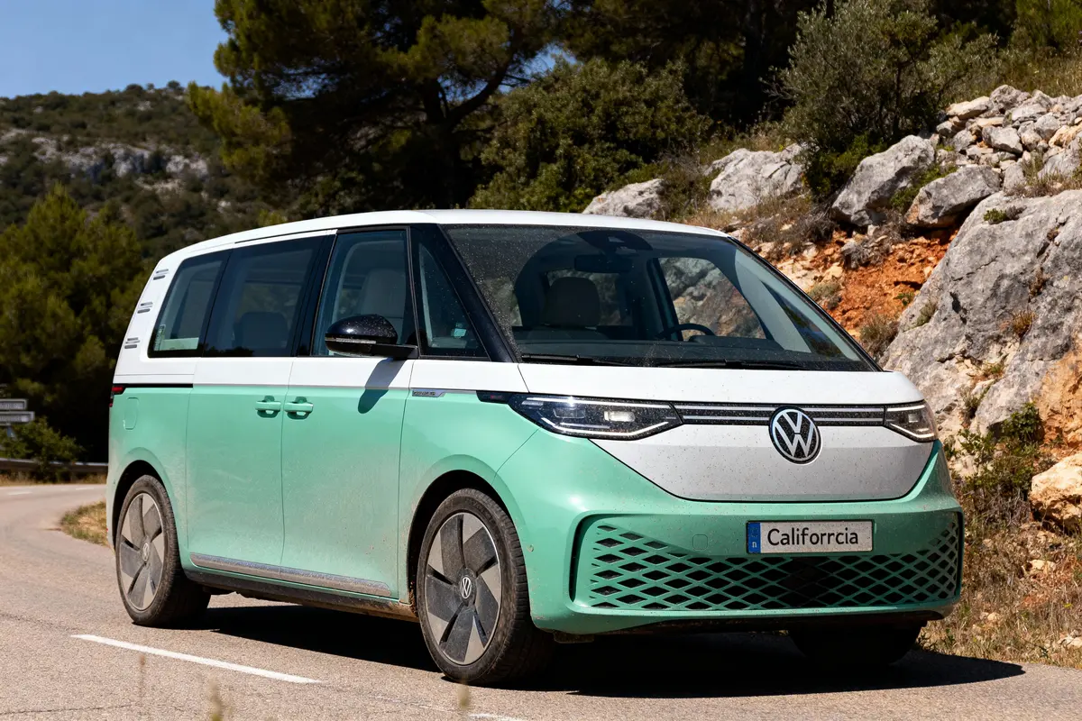 Combi Volkswagen bicolore stationné sur route sinueuse, environnement naturel avec arbres et rochers en arrière-plan.