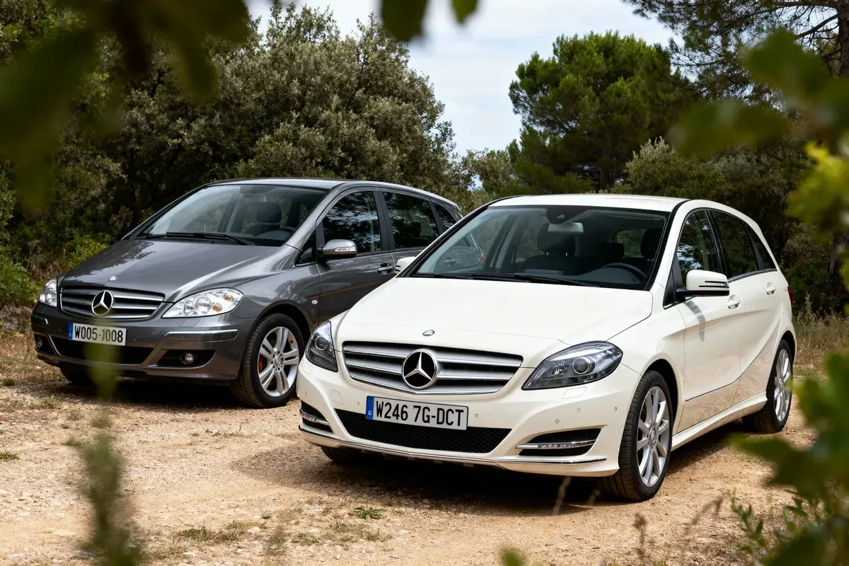 Deux Mercedes-Benz garées en extérieur, une blanche et une grise, entourées d'arbres.