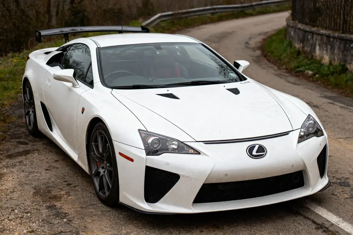 Voiture de sport blanche stationnée sur route de campagne sinueuse avec aileron arrière.