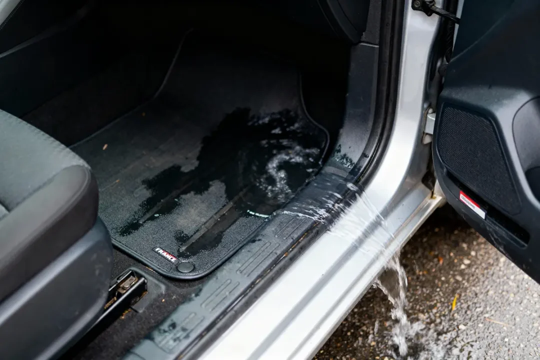 Tapis de voiture inondé, eau s'écoulant par la portière ouverte, intérieur détrempé.