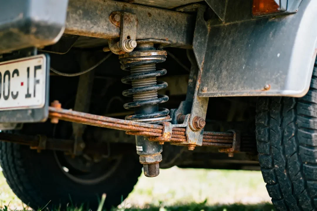 Suspension de voiture rouillée montrant un ressort hélicoïdal et une plaque d'immatriculation partiellement visible.
