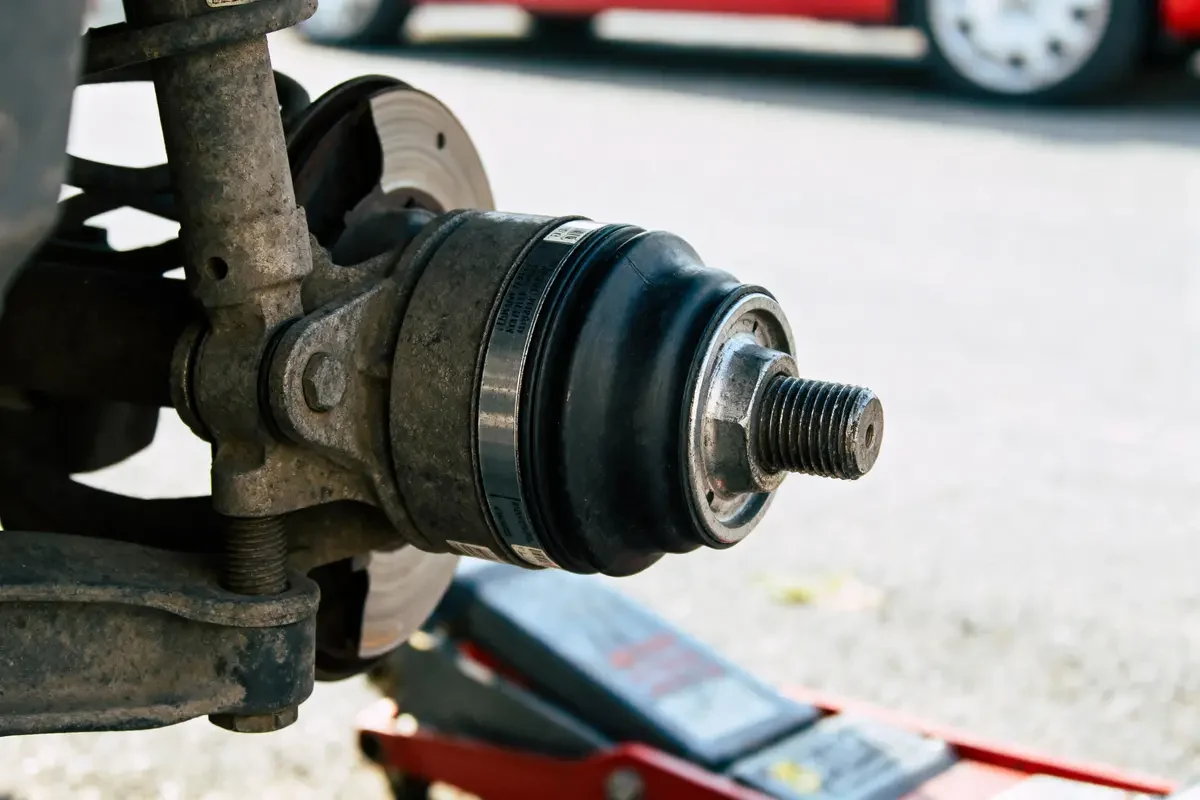 Suspension de voiture avec rotule visible, partiellement démontée, montrant amortisseur et disque de frein en arrière-plan.