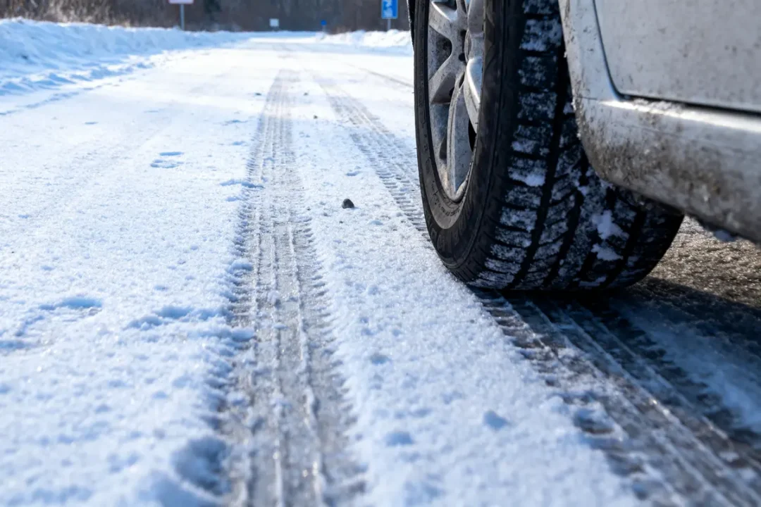 Voiture roulant sur route enneigée, traces de pneus visibles sur la neige.