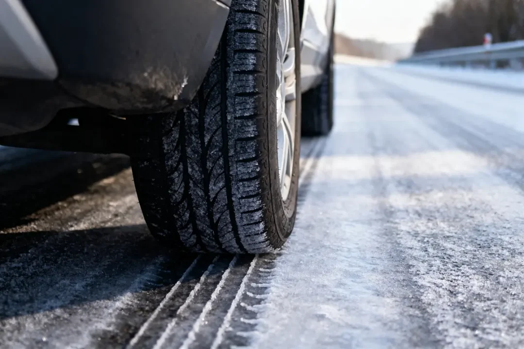 Pneu de voiture roulant sur une route enneigée et glacée en hiver, vue rapprochée.
