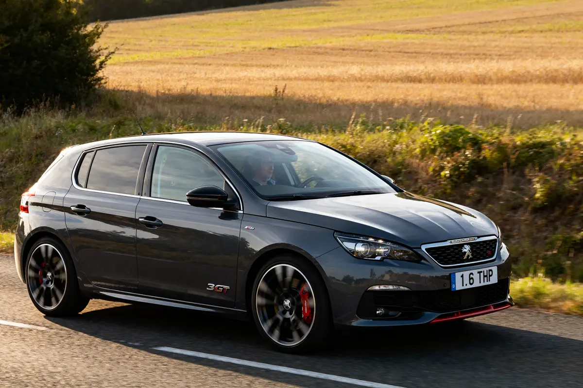 Voiture Peugeot 308 GTi grise roulant sur route de campagne ensoleillée