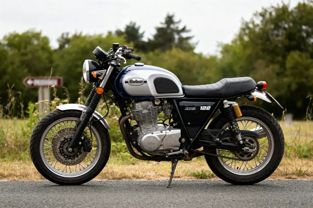 Moto rétro Bobber 125 stationnée sur une route en campagne verdoyante