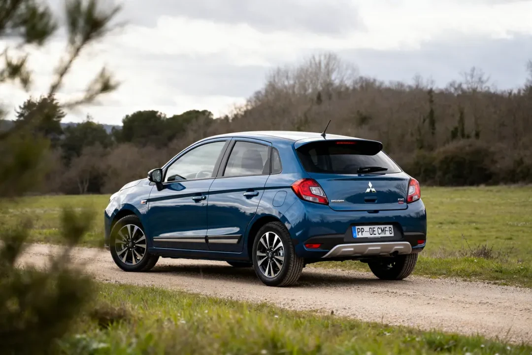 Voiture Mitsubishi Colt bleu stationnée sur chemin de terre devant paysage naturel