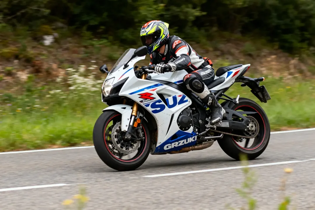 Un motard conduit une Suzuki GSXR blanche sur une route de campagne.