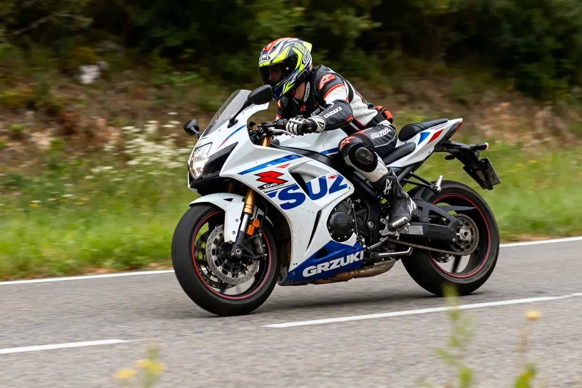 Un motard conduit une Suzuki GSXR blanche sur une route de campagne.
