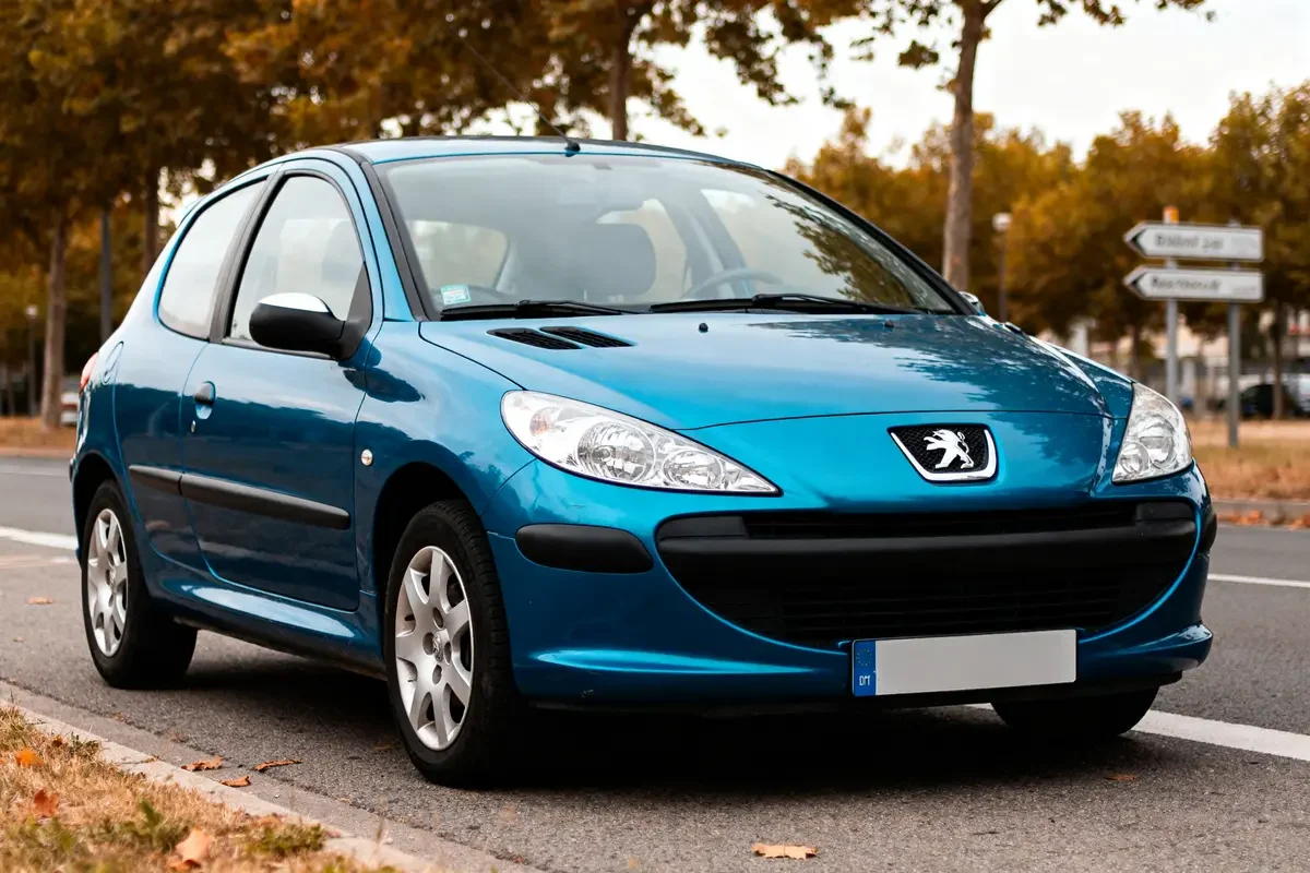 Voiture hatchback Peugeot 206 bleue garée sur une route bordée d'arbres