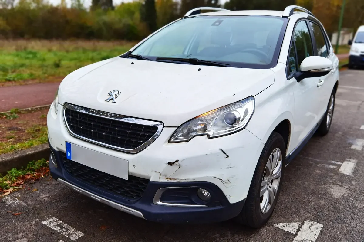 SUV blanc Peugeot en stationnement avec rayures sur le pare-chocs avant, modèle 2008 à éviter