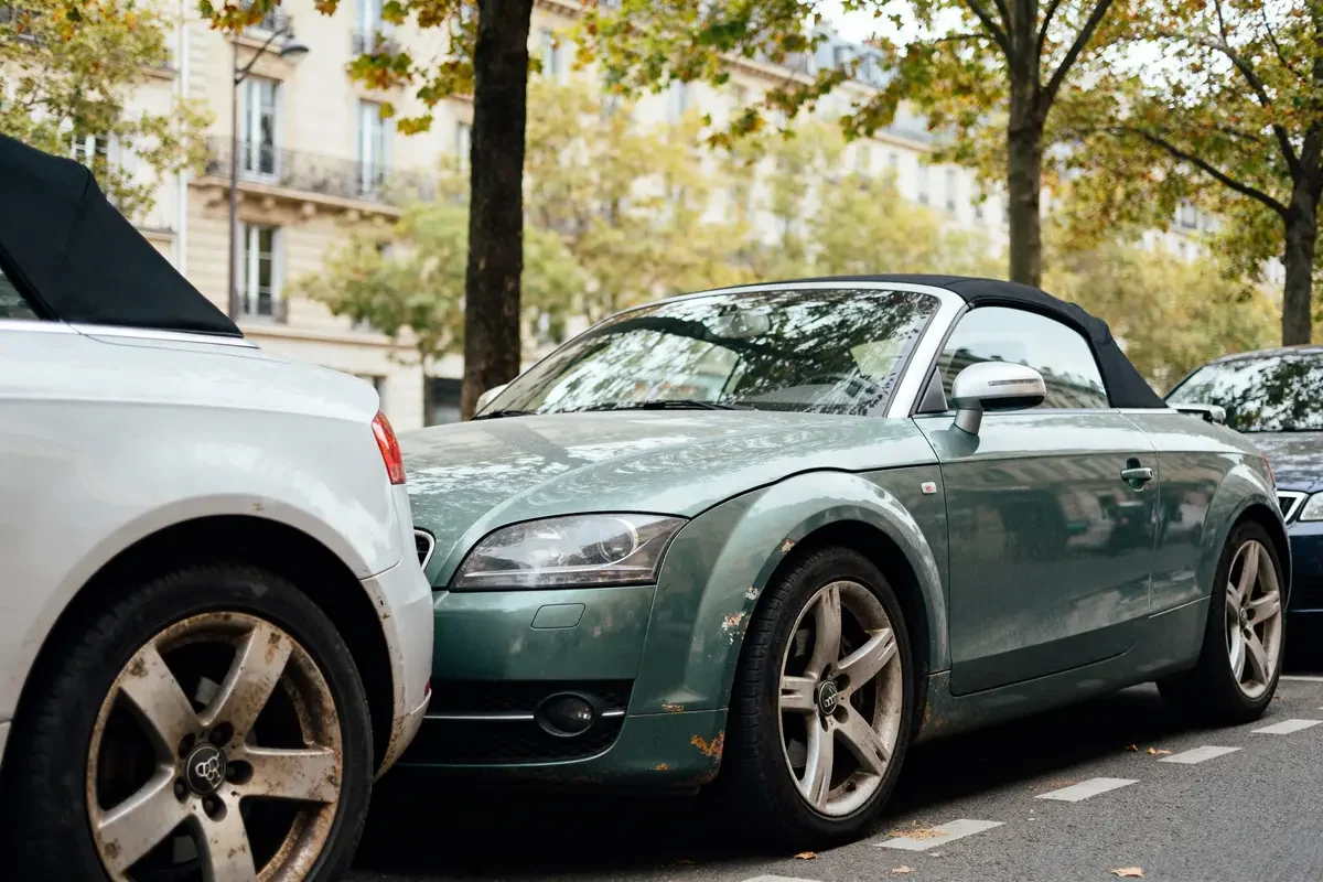 Audi TT vert d'occasion garée en ville sous les arbres en automne
