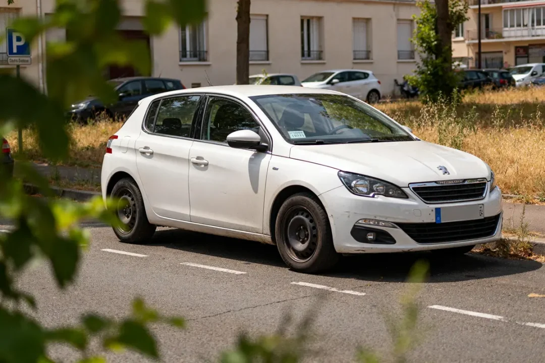 Voiture blanche garée avec contrôle technique périmé depuis 1 mois visible sur le pare-brise