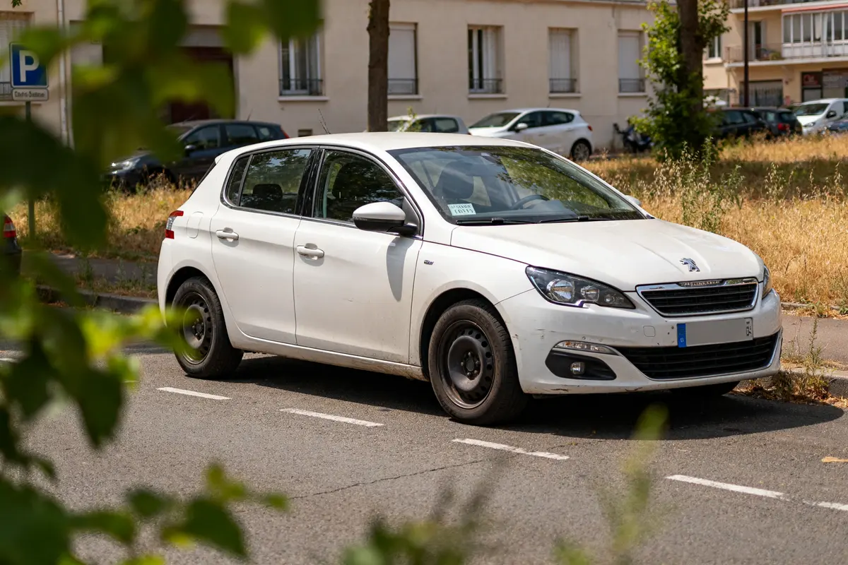 Voiture blanche garée avec contrôle technique périmé depuis 1 mois visible sur le pare-brise