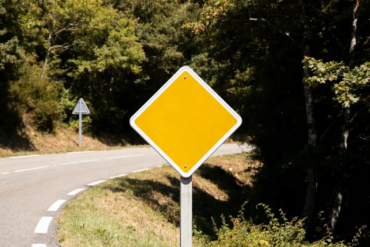 Panneau losange jaune indiquant une priorité sur route sinueuse boisée avec virage visible