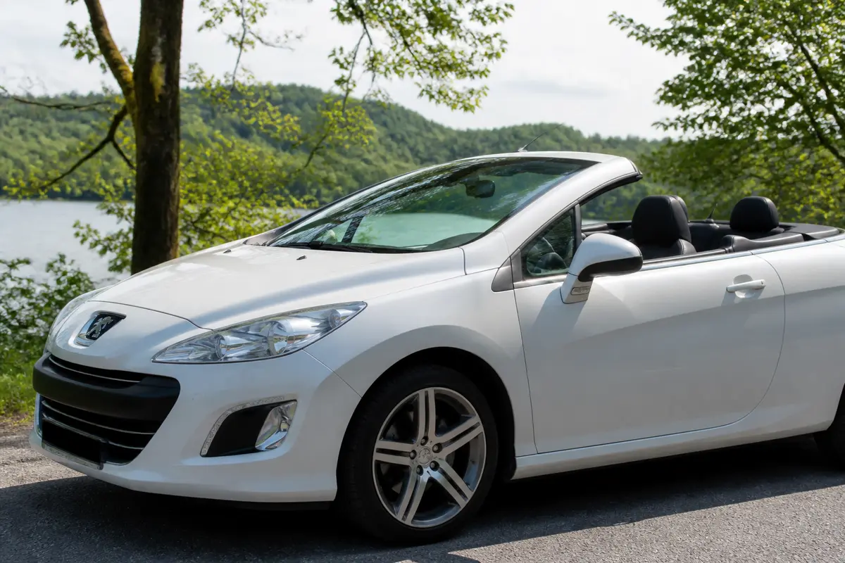 Voiture blanche cabriolet Peugeot 308CC garée devant un paysage verdoyant.