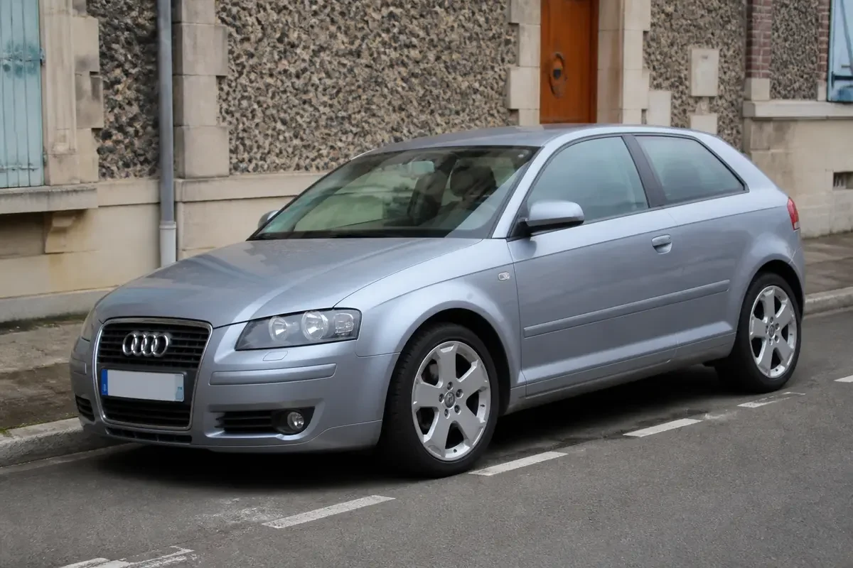Voiture Audi A3 8P grise garée en ville devant un mur de pierres